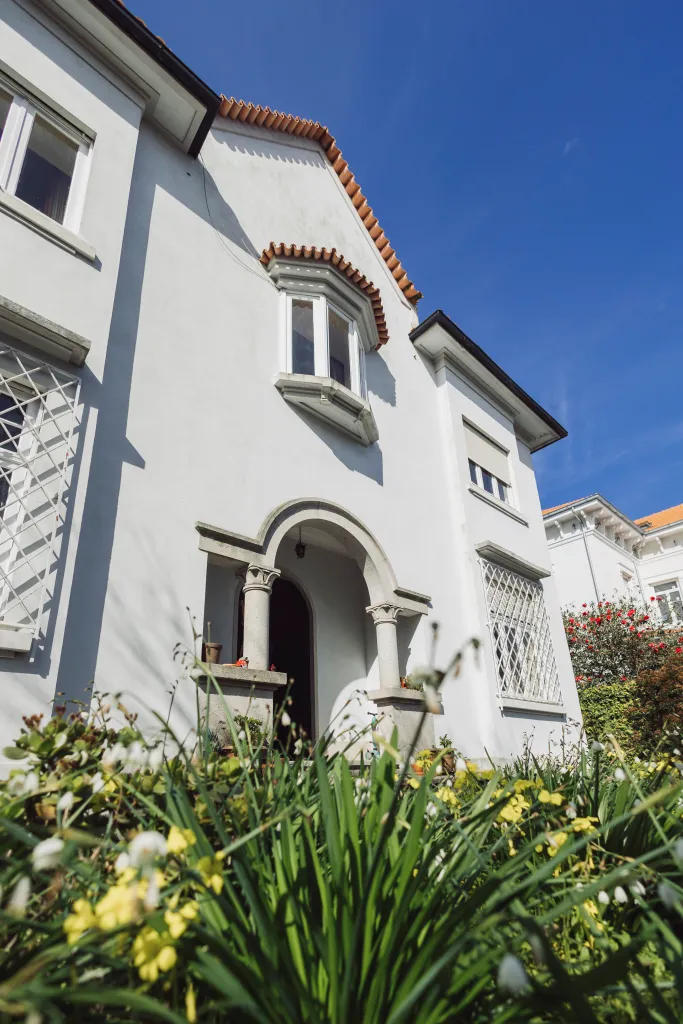 Fachada branca da casa da Escola Normal no Porto com jardim à frente