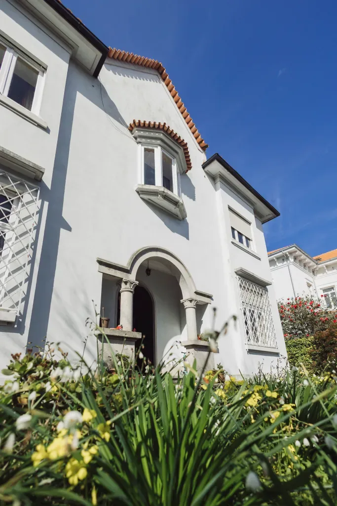 Fachada branca da casa da Escola Normal no Porto com jardim à frente